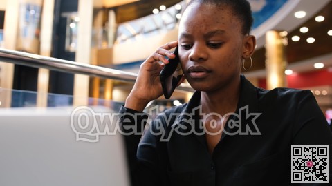 An African woman works at a computer and talks on the phone while typing on the keyboard.
