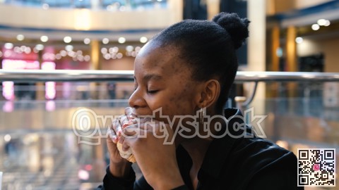 Young african american woman eating fast food in a restaurant enjoying delicious juicy burger