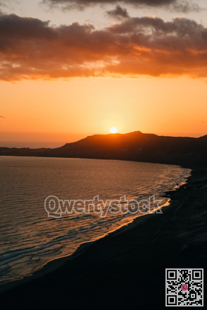 Vivid sunset with coastal silhouette. Dramatic dusk with layered clouds reflecting in calm waters