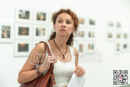Middle-aged woman looking at pictures on wall in museum