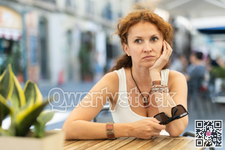 Thoughtful middle-aged woman sitting in open-air cafe