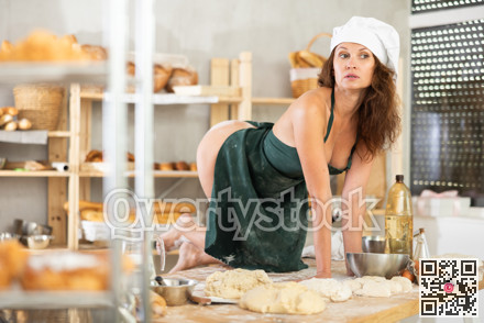 Sexy female baker in apron on naked body posing sexy on knees on kitchen table of bakery