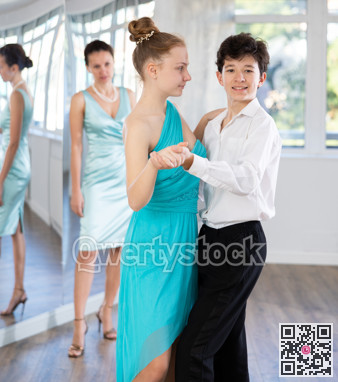 Girl and a boy in festive clothes learn to dance tango under guidance of teacher