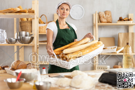 Positive young woman baker in uniform baking fresh baguettes in bakery