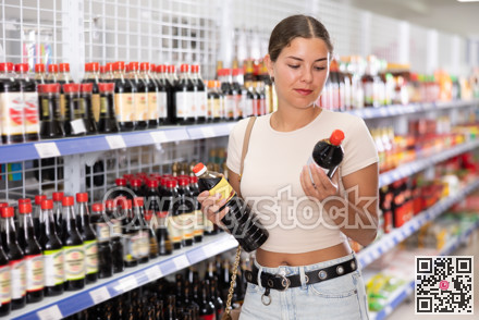 Young woman choosing soy sauce in store