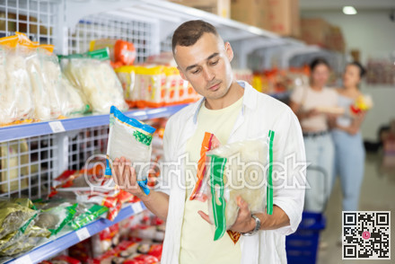 Pensive shopper choosing Asian noodles at grocery store