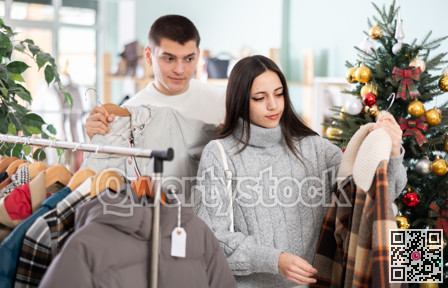 Young couple choosing coat or jacket for girl in clothing store