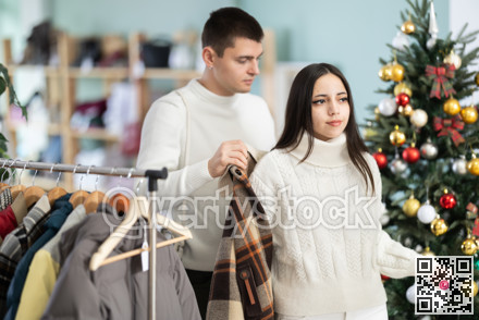 Girl tries on plaid jacket accompanied by guy in shop, X mas eve
