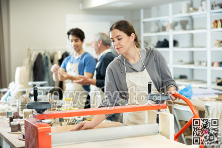 Young woman rolling raw clay with mechanical slab roller