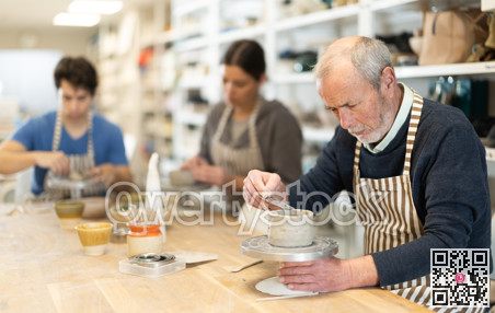 Mature man at table molds cup from wet clay in pottery workshop