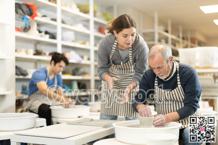 Girl help to mature man working on potters wheel in pottery workshop