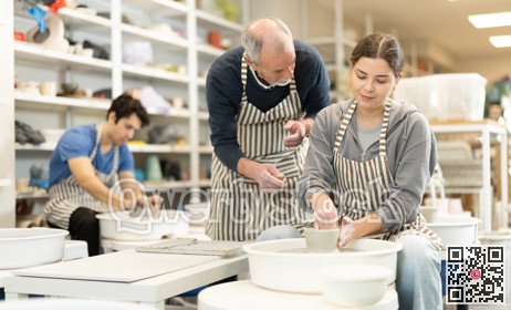 Mature man help to girl working on potters wheel in pottery workshop