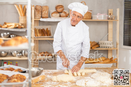 Baker in uniform cutting raw dough with knife to make croissants or buns