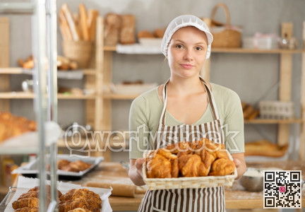 Smiling young female baker holding tray of croissants
