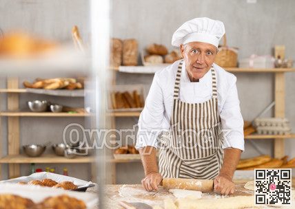 Senior male baker works with rolling pin, rolls out and spreads out pieces of dough