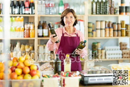 Experienced female salesperson offers choice of buying bottle of vegetable oil or olive oil in grocery store