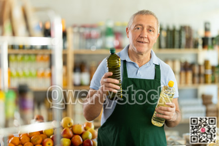 Elderly man seller offers vegetable oil in grocery store