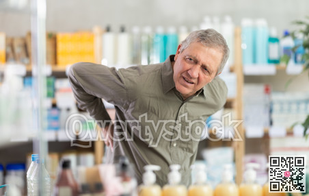 Older man experiencing sharp back pain while shopping in pharmacy