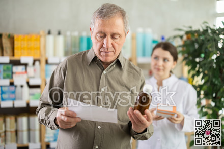 Elderly male customer chooses cough syrup in modern pharmacy. Female pharmacist helps with choosing medicine