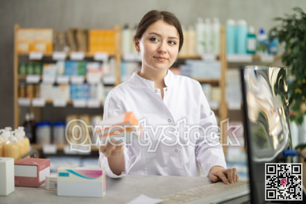 Female pharmacist standing at drugstore with medical product in hands
