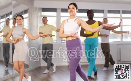 Happy young woman and group of multinational people enjoying active boogie-woogie dance in studio
