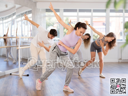 Cheerful young girl and multinational people training synchronous group choreography in dance studio
