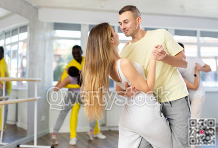 Happy active pair with multinational young men and women dancing and training latin dance movements in ballroom together