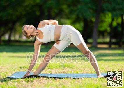 Girl in park on green grass of lawn performs Trikonasana, triangle asana