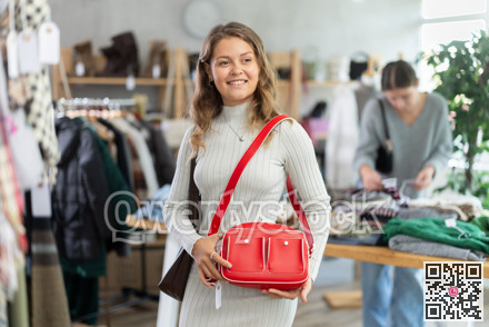 Positive young girl choosing handbag in clothing store