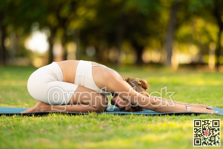 Young woman doing restful yoga pose Balasana in summer park