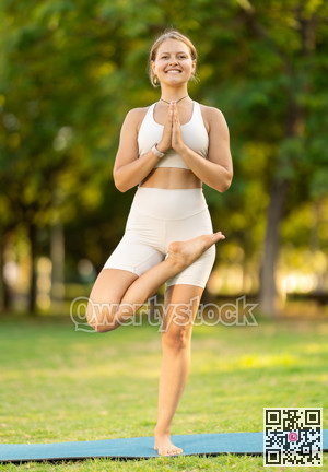 Girl in park on green grass of lawn performs Ardha Baddha Padma Vrikshasana