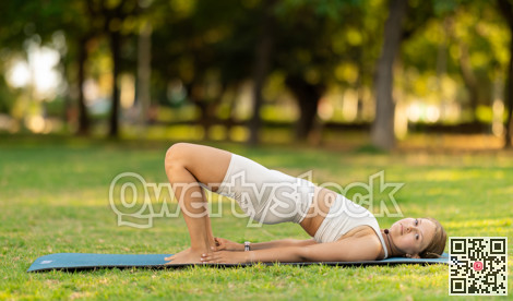 Girl in park on green grass of lawn performs Setu Bandha Sarvangasana