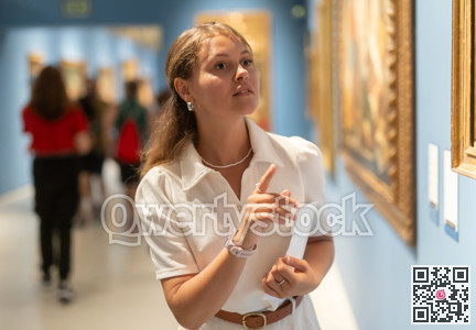 Portrait of young girl visitor with paper guide at the exhibition of paintings in museum