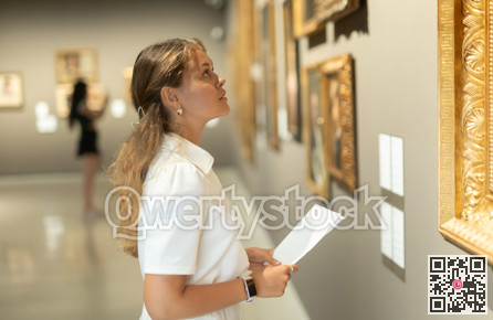 Woman with sheet piece of paper in hands view pictures and icons in museum hall