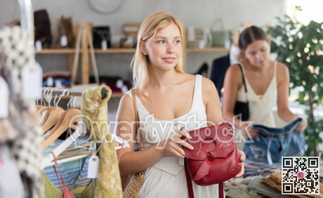 Young woman choosing a handbag against the background of a buyer