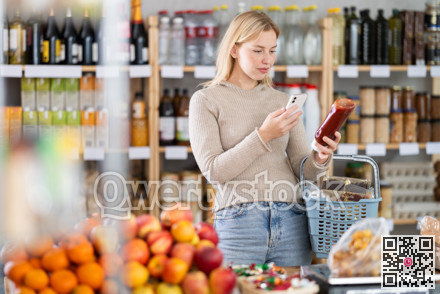 Female shopper scanning QR code on bottle ketchup label in grocery department of shop