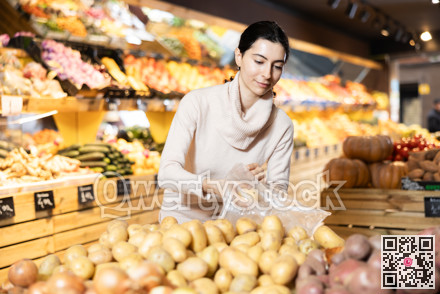 In vegetable store, young woman customer buy ripe potato