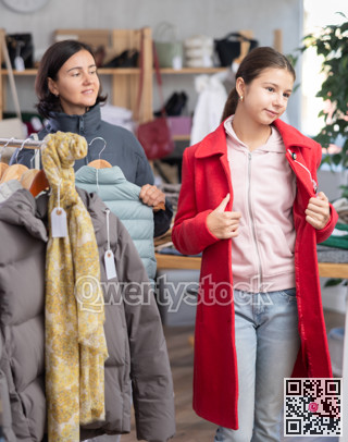 Adolescence girl try on red coat during shopping with mother in clothes store