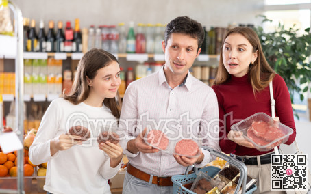 Dad, mom and daughter choose raw chilling beef entrecote and semi-finished hamburger cutlet in shop