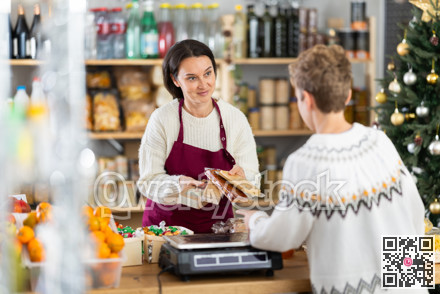 Female salesperson offers to buy nougat to teenage boy in Christmas interior of grocery supermarket