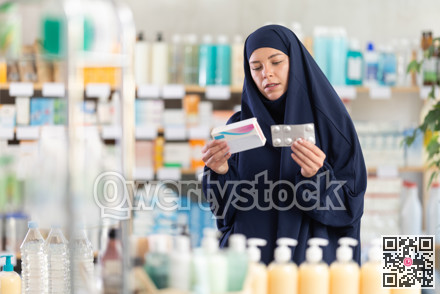 Young woman in khimar examining medicine box at pharmacy