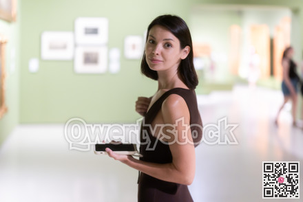 Woman with phone in hands in museum hall, view painting exhibition