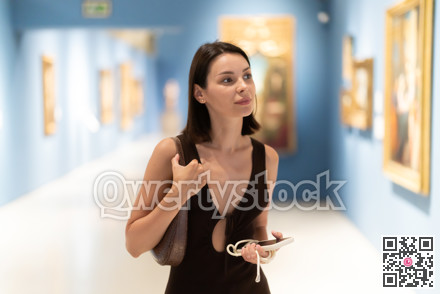 Young woman in summer clothes looking at paintings in museum