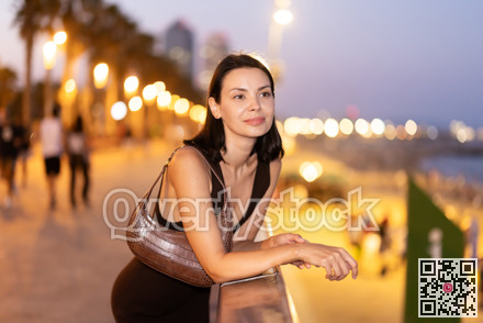 Young woman leaning on parapet at Barceloneta beach in summer evening