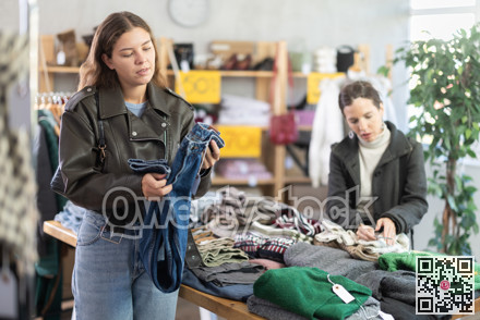 Attentive young girl choosing jean pantaloons in clothing store
