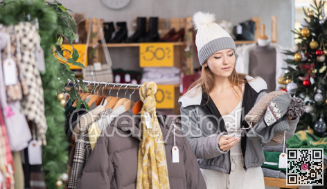 Girl client looks at products in store, looks closely at hat, picks up wardrobe item