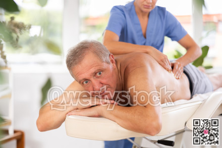 Relaxed old man having back massage therapy conducted by skilled masseuse