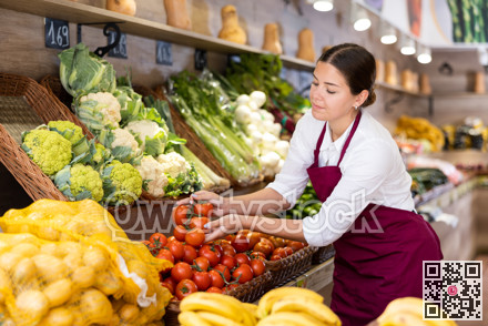 Young female seller laying out tomatoes on display in store