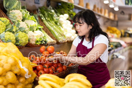 Young saleswoman placing tomatos on food stall in grocery store