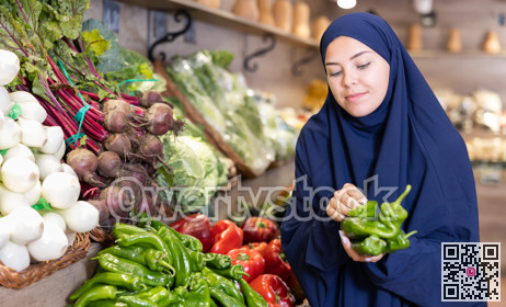 Young european woman in muslim abaya and chador choosing peppers in store